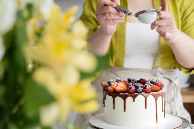 Photo by SHVETS production: https://www.pexels.com/photo/crop-female-baker-strewing-powdered-sugar-to-decorated-cake-7525173/ -- event vendor baker