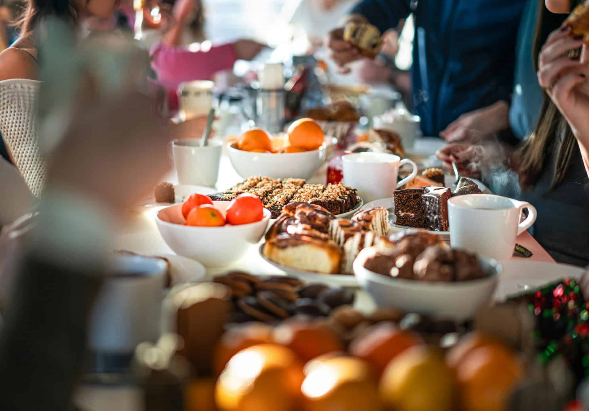 Coworkers enjoying a vibrant team-building dinner with coffee, pastries, fruits, and desserts on a shared table.