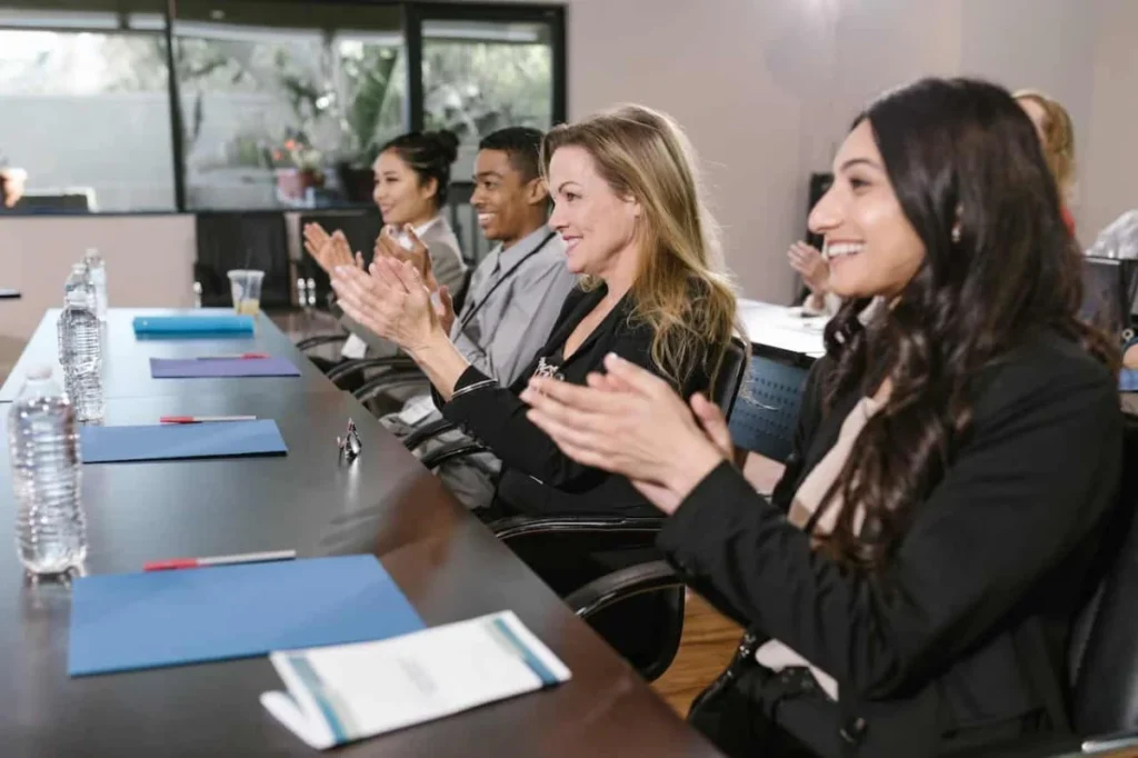 Photo by RDNE Stock project: https://www.pexels.com/photo/group-of-people-in-a-conference-room-clapping-their-hands-7648045/ -- corporate meeting