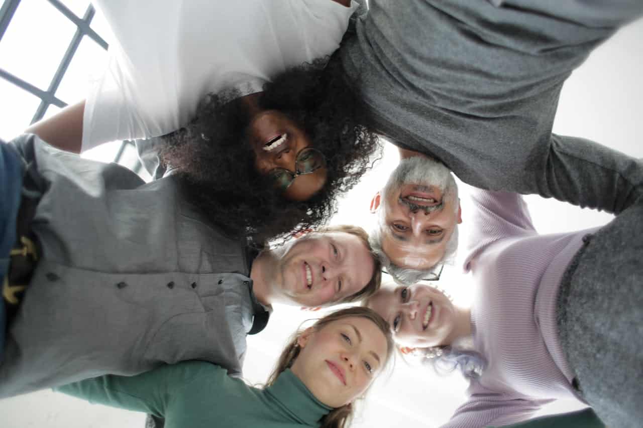 Image title: team-building Image alt-title: Multi-ethnic coworkers in a circle during a team building event. Image URL: https://www.pexels.com/photo/from-below-of-cheerful-multiethnic-coworkers-embracing-each-other-in-circle-during-team-building-in-office-3931556/ 