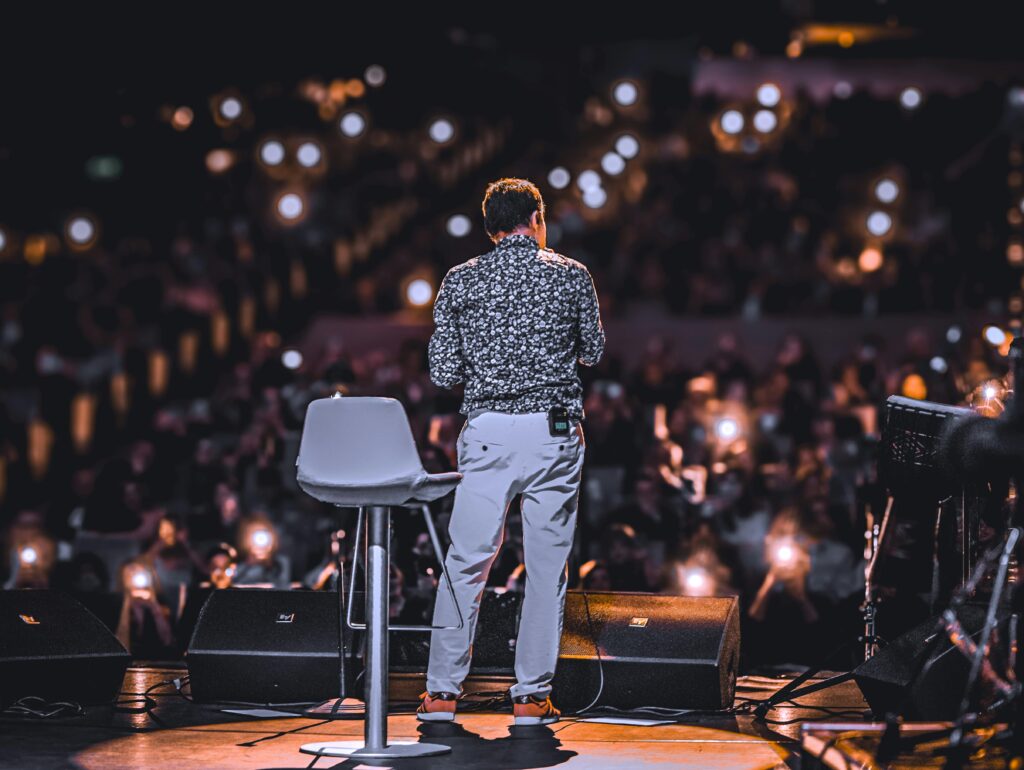 Photo by Kerim Isazade: https://www.pexels.com/photo/back-view-of-speaker-on-stage-with-audience-lights-31129059/