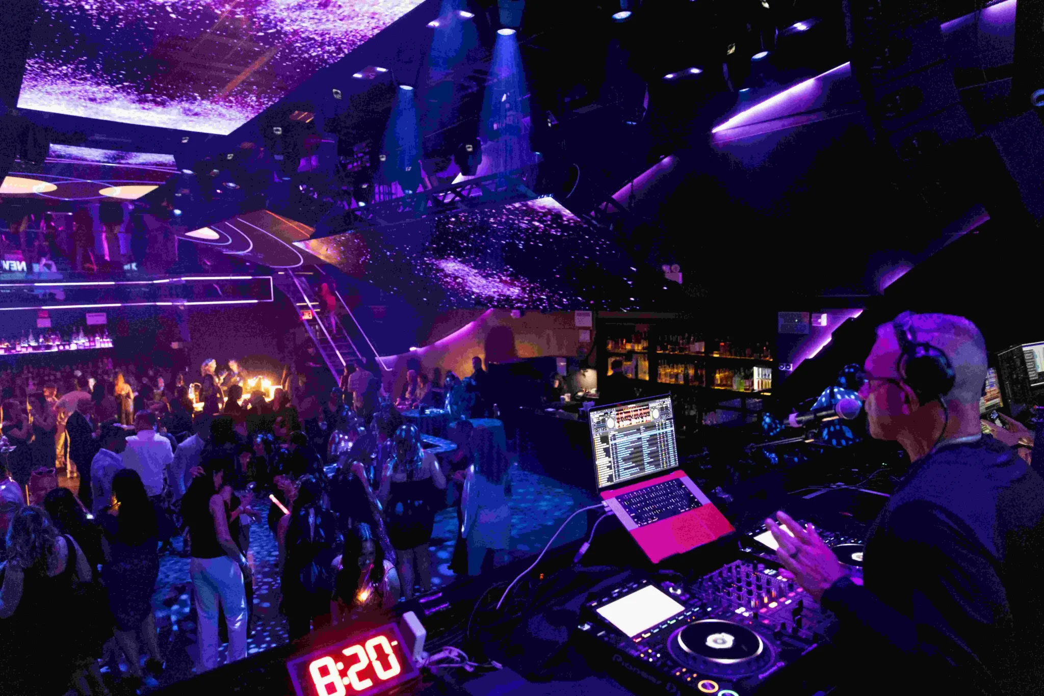 DJ performing at a purple-lit NYC nightclub with a full dance floor, EMRG Media