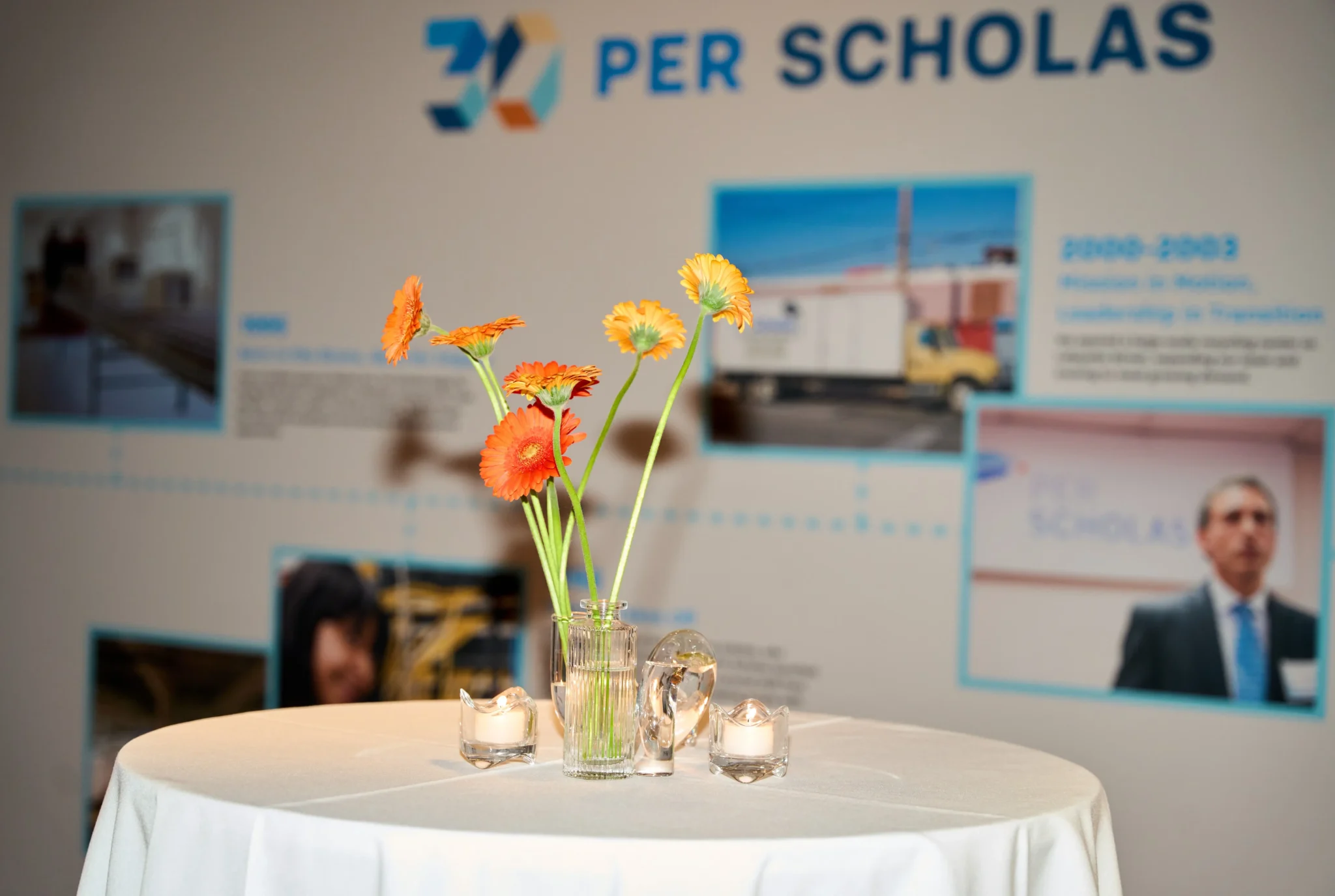 Orange gerbera daisy centerpiece in front of Per Scholas's 30th anniversary timeline display at a NYC event, EMRG Media