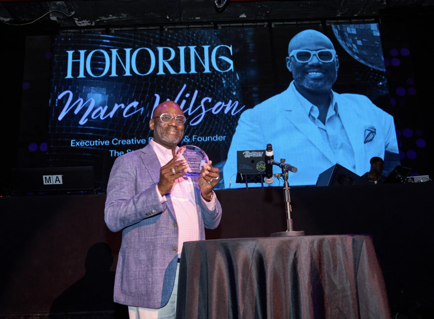Marc Wilson accepting an award on stage at a NYC honoree ceremony, photographed by EMRG Media